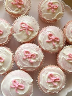 many cupcakes with pink bows on them are sitting on a white platter