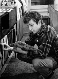 a young man sitting on the floor reading a book next to an old record player