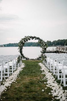 an outdoor ceremony setup with white flowers and greenery on the aisle, overlooking water