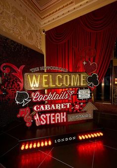 a welcome sign is lit up in front of a red drapeed curtain and floor