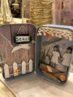 two tins that have pictures inside of them on a table with other items in the background