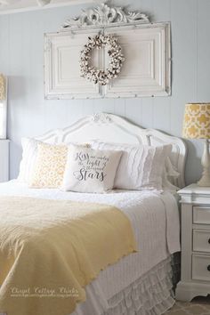 a white bed topped with pillows and a wreath on the wall above it's headboard