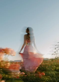 a blurry photo of a woman in a pink dress walking through some bushes and flowers