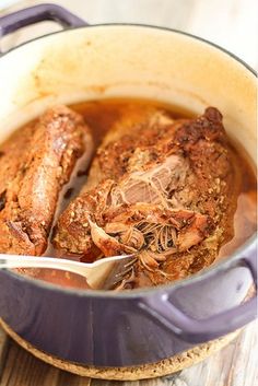 two meats are being cooked in a pot with a spoon on the table next to it