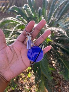 a person's hand holding a blue heart shaped keychain in front of a palm tree