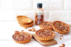 three pecan pies on a cutting board next to a bottle of maple syrup