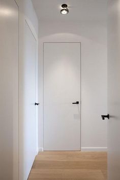 an empty white room with two doors and some lights on the wall above it, along with wood flooring