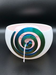 a white bowl with blue and green swirls on the outside, sitting on a black surface