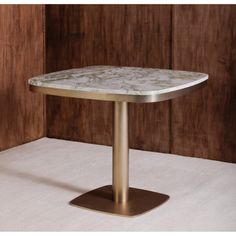 a white marble top table with gold metal pedestals on carpeted floor next to wooden wall