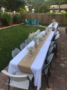 a long table set up with flowers and candles for an outdoor dinner in the back yard