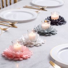 three candles sitting on top of a table with white plates and gold forks in front of them