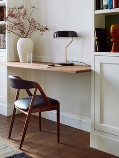 a desk with a chair, lamp and vase on it