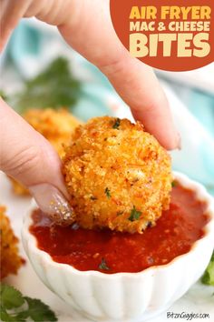 a person dipping something into a small bowl filled with sauce and breaded meatballs