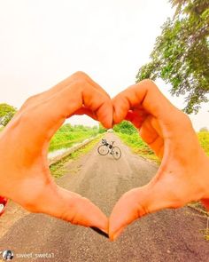 two hands making a heart shape with a bicycle in the background on a country road