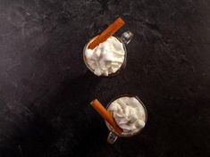 two glasses filled with whipped cream and cinnamon sticks on top of a black countertop