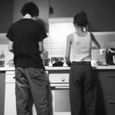 two people are standing in the kitchen preparing food on the stove top and looking at something off to the side