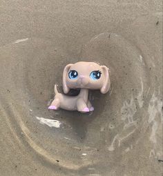 a toy elephant with blue eyes sitting in the sand at the ocean's edge