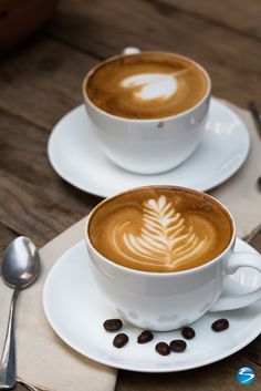 two cups of cappuccino on saucers with spoons