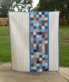 a blue and white quilt hanging from the side of a pole in front of some grass