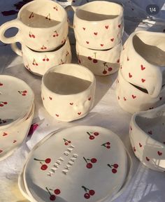 a table topped with lots of white dishes and cups filled with cherries on them