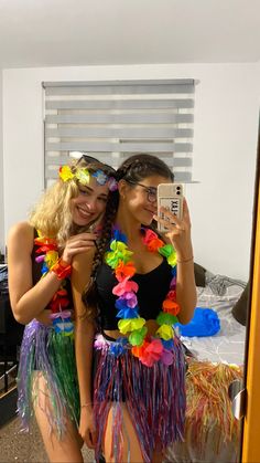 two women dressed in colorful hula skirts taking a selfie with their cell phone