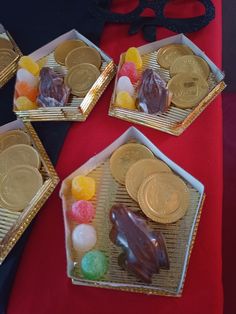 four small trays filled with different types of candies and coins on top of a red table cloth