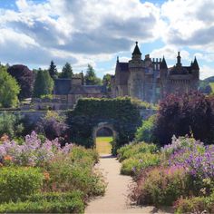 an old castle with lots of flowers in the foreground and a path leading to it