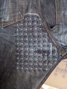 the back pocket of an old pair of jeans with blue crosses on it, next to a ruler