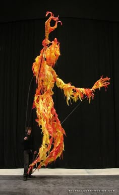 a man standing in front of a giant orange and yellow fire dragon kite on top of a stage