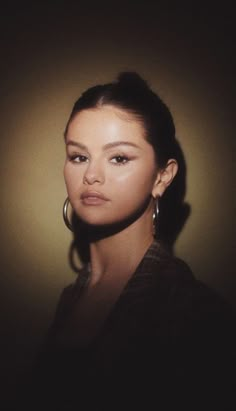 a woman with large hoop earrings on her ear looking at the camera while standing in front of a wall