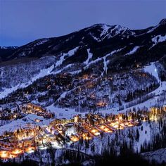 the town is lit up at night in the snow covered mountain range with lights on it