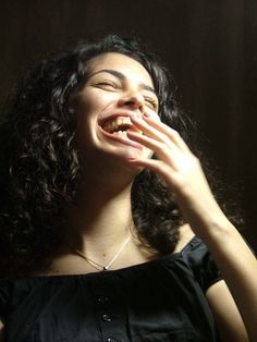 a woman with curly hair is smiling and holding her hand to her mouth