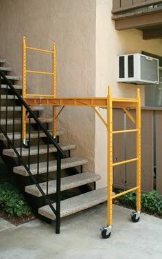 a yellow ladder next to a building with a microwave on the wall and stairs in front