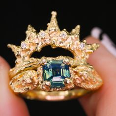 a close up of a person's hand holding a ring with an emerald colored stone