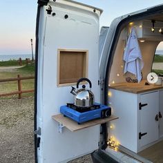 an open camper door with a tea kettle on the stove and lights in the back