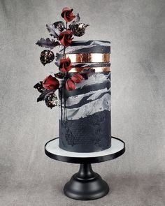 a three tiered cake decorated with flowers and leaves on a black metal stand against a gray background