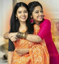 two women are hugging each other in an orange and pink sari with red accents