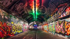 a tunnel with graffiti all over it and a green light at the end is lit