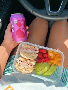 a person is holding a pink soda and some food in their lap while sitting down