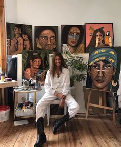 a woman sitting on a chair in front of some paintings and other art work behind her