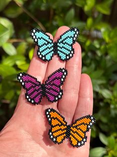 three small beaded butterflies sitting on someone's hand in front of some bushes