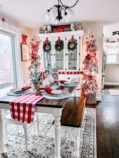 a dining room table decorated for christmas with red and white decorations on the wall, wreaths hanging from the back