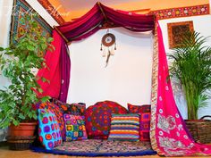 a couch covered in colorful pillows next to a potted plant and hanging dream catcher