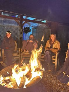 four people sitting around a fire pit at night