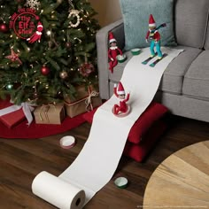 a christmas tree with elf figurines next to a roll of paper on the floor