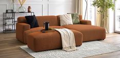 an orange couch sitting on top of a wooden floor next to a white rug and window