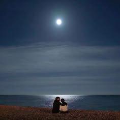 two people sitting on the beach watching the moon