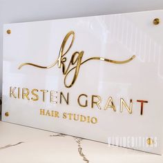 a white sign with gold lettering that says kristen grant hair studio on it