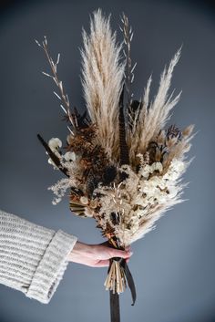 a bouquet of dried flowers being held by a person's hand in front of a gray background