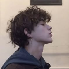 a young man with curly hair is staring off into the distance while standing in front of a wall